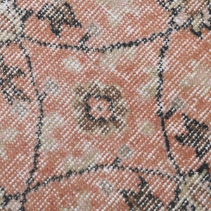 May include: Close-up of a pink and brown patterned rug with a woven texture. The rug has a geometric design with repeating shapes.