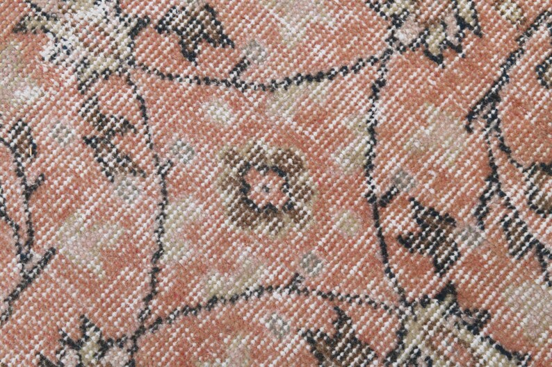 May include: Close-up of a pink and brown patterned rug with a woven texture. The rug has a geometric design with repeating shapes.