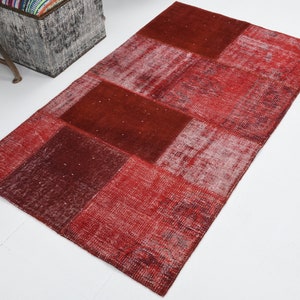 May include: Red patchwork rug with a distressed look. The rug is made of different pieces of fabric sewn together. It has a rectangular shape and is made of wool.