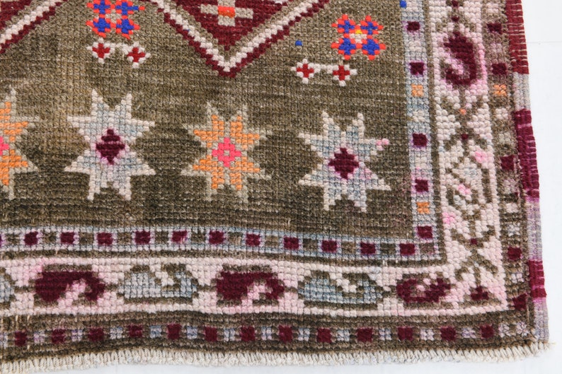 K&ouml;nnte beinhalten: Ein brauner Teppich mit einem geometrischen Muster in den Farben Rosa, Rot, Orange und Blau. Der Teppich hat einen Fransenrand.