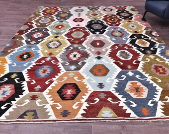 Può includere: Un grande tappeto rettangolare con un motivo geometrico. Il tappeto presenta un motivo ripetuto di forme esagonali colorate nelle tonalità di rosso, blu, arancione, nero e bianco. Il tappeto è posto su un pavimento in legno.