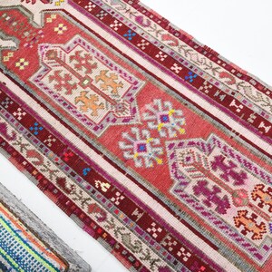 K&ouml;nnte beinhalten: Ein langer, schmaler Teppich mit traditionellem t&uuml;rkischem Design. Der Teppich ist haupts&auml;chlich rot mit wei&szlig;en, rosa und blauen Akzenten. Das Design zeigt komplizierte geometrische Muster und florale Motive.
