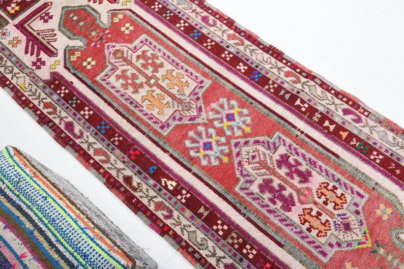 K&ouml;nnte beinhalten: Ein langer, schmaler Teppich mit traditionellem t&uuml;rkischem Design. Der Teppich ist haupts&auml;chlich rot mit wei&szlig;en, rosa und blauen Akzenten. Das Design zeigt komplizierte geometrische Muster und florale Motive.
