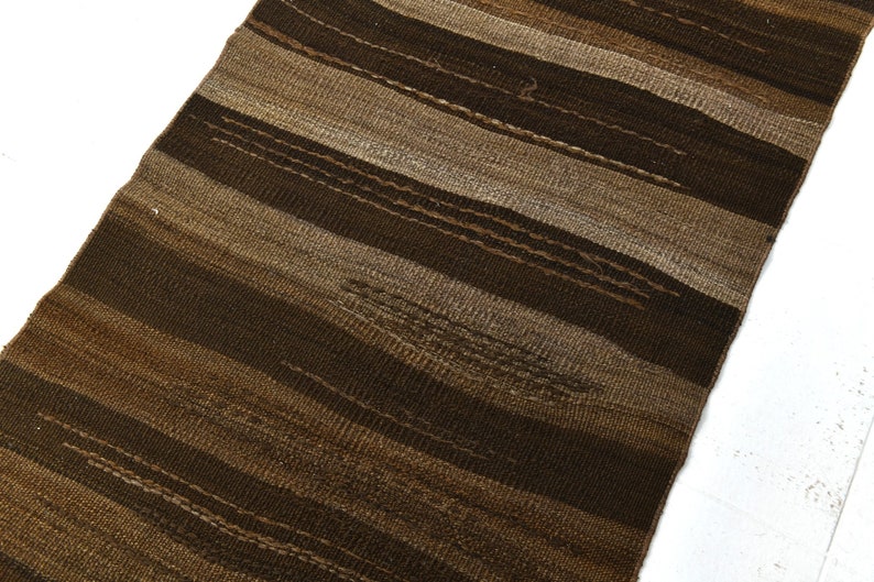 May include: A brown and beige striped woven rug with a textured surface.