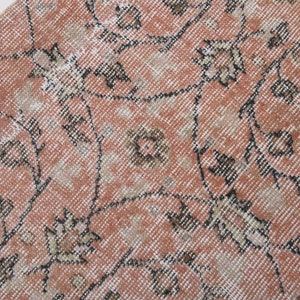 May include: A vintage rug with a floral pattern in shades of pink, brown, and white. The rug has a distressed look and is made of a soft, woven material.