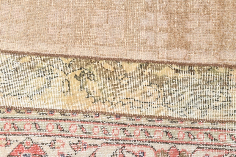 May include: Close-up of the bottom edge of a rug with a beige background and a patterned border. The border features a repeating design of pink, green, and brown.