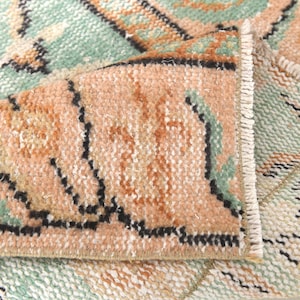 May include: Close-up of a woven rug with a pink, green, and white geometric pattern. The rug has a fringe border.