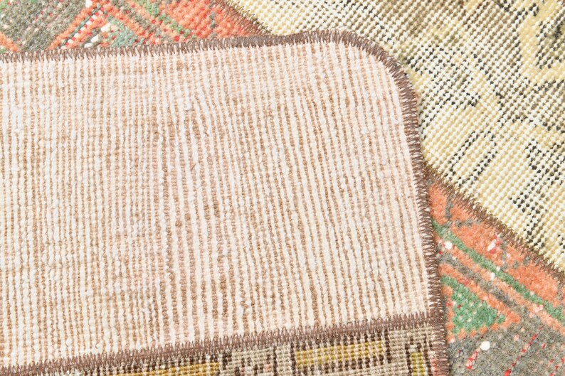 May include: Close-up of a beige and brown woven rug with a textured surface. The rug has a stitched edge and is made of different pieces of fabric.
