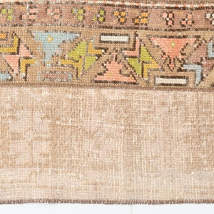 May include: Close-up of the bottom edge of a vintage rug with a brown fringe. The rug has a light brown background with a colorful geometric pattern.