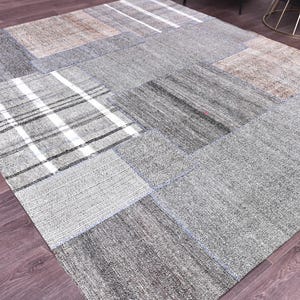May include: A rectangular patchwork rug with a variety of gray and tan fabric squares. Some squares have white stripes or patterns. The rug is on a wooden floor.