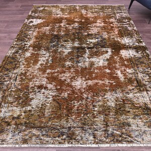 May include: Rectangular area rug with a distressed, vintage appearance. The rug features a blend of brown, white, and green hues, with a central pattern and a darker border. The rug is placed on a wooden floor.