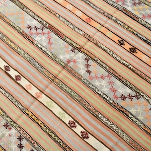 May include: A traditional Turkish kilim rug with a striped pattern in shades of pink, beige, brown, and gray. The rug features intricate geometric designs woven into the fabric.