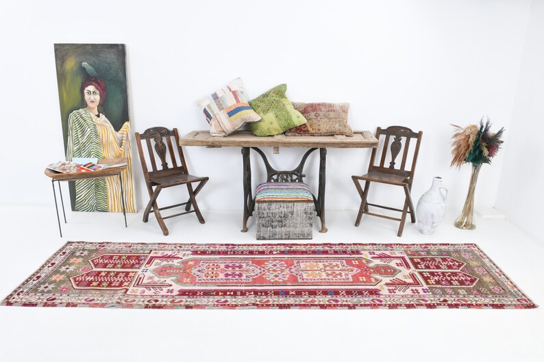 K&ouml;nnte beinhalten: Ein Vintage-L&auml;ufer mit einem geometrischen Muster in Rot, Rosa und Wei&szlig;. Der L&auml;ufer liegt auf einem wei&szlig;en Boden in einem Raum mit einem Holztisch, zwei St&uuml;hlen und einem Gem&auml;lde an der Wand.