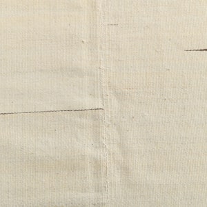 May include: Close-up of a plain, off-white fabric with a subtle texture. The fabric has two horizontal seams running across it.