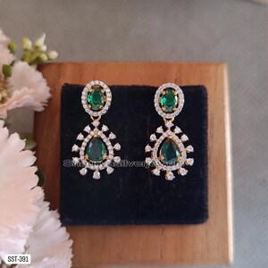 Pu&ograve; includere: Un paio di orecchini pendenti color oro con accenti di smeraldo verde e cristalli trasparenti. Ogni orecchino presenta una pietra verde ovale circondata da cristalli trasparenti nella parte superiore e una pietra verde a forma di pera nella parte inferiore.