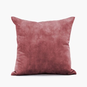Pode incluir: Uma almofada de veludo vermelho macio com um padrão texturizado sutil. A almofada é de forma quadrada e tem um design simples e elegante.