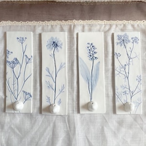 May include: Four white ceramic tiles with blue floral designs. Each tile has a small white knob at the bottom.