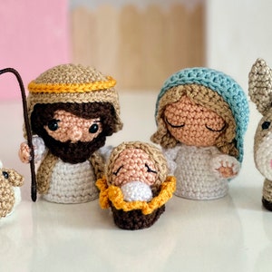 Könnte beinhalten: Häkel-Krippe mit einem braunen Esel, einem weißen Schaf, einem Jesuskind in einer Krippe, Maria mit einem blauen Kopftuch und Josef mit einem gelben Heiligenschein.