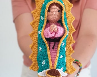 May include: Crocheted amigurumi doll of the Virgin Mary, wearing a blue and gold robe with white stars. The doll is holding her hands in prayer and has a sweet, gentle expression.