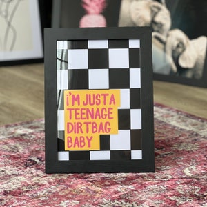 May include: Black framed print with a black and white checkered background. A yellow rectangle with pink text reads "i'm just a teenage dirtbag baby".