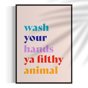 Puede incluir: Una l&aacute;mina de arte enmarcada con fondo beige claro y el texto "wash your hands ya filthy animal" impreso en cinco l&iacute;neas. La palabra "wash" es verde azulado, "your" es azul oscuro, "hands" es morado claro, "ya filthy" es rojo y "animal" es naranja.