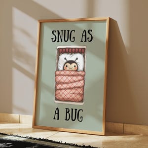 Peut inclure: Une affiche encadrée avec le texte "SNUG AS A BUG" au-dessus d'une illustration de dessin animé d'un personnage d'abeille au lit. L'abeille est sous une couette rose et blanche, sur un oreiller blanc, dans un cadre de lit rectangulaire.