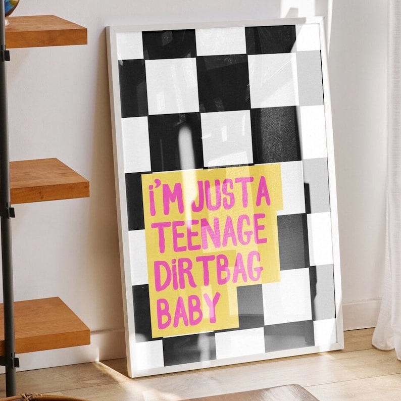 May include: A framed print with a black and white checkered background. The print features a yellow rectangle with the text "i'm just a teenage dirtbag baby" in pink letters.