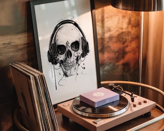 Puede incluir: Una ilustración en tinta blanca y negra enmarcada de un cráneo humano con auriculares, expuesta junto a una pila de discos de vinilo y un tocadiscos con una pequeña caja morada descansando sobre el plato giratorio.