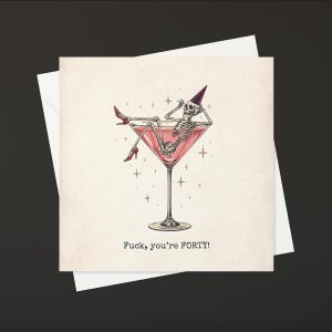 May include: A greeting card with a humorous illustration. A skeleton wearing a party hat and red high heels reclines in a pink martini glass. The text "Fuck, you're FORTY!" is printed below the image.