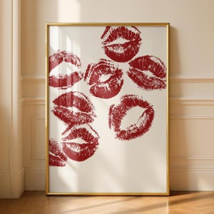 May include: A framed print displaying several red lipstick kiss marks against an off-white backdrop. The artwork is encased in a gold-coloured frame, enhancing its visual appeal. This print is a decorative item.