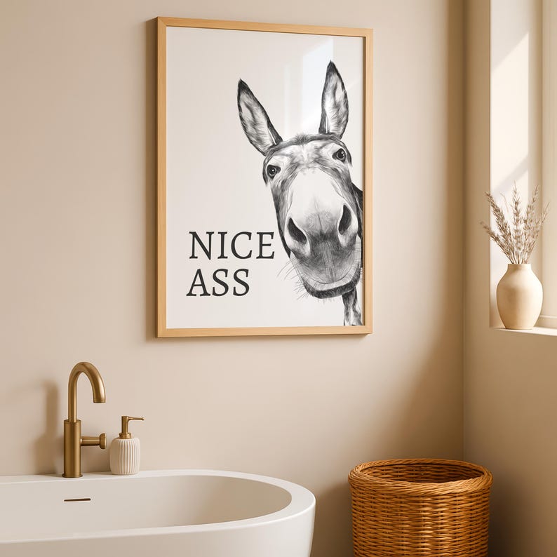 May include: A framed wall art print featuring a black and white charcoal-style illustration of a donkey head looking forward. The text NICE ASS is printed in black capital letters on the left side of the white background within a light wood frame.