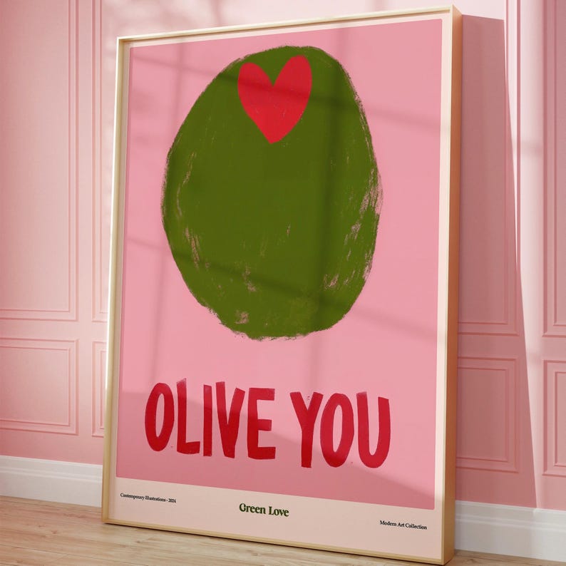 May include: A framed art print featuring a large green olive with a red heart on a pink background. Bold red text reads "OLIVE YOU". Below the text are the words "Green Love" and "Modern Art Collection".