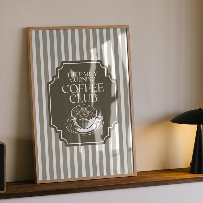 May include: Framed print featuring a coffee-themed design. The artwork has a brown and white striped background with a central label that reads "THE EARLY MORNING COFFEE CLUB." The label includes a coffee cup illustration. The frame is made of wood.
