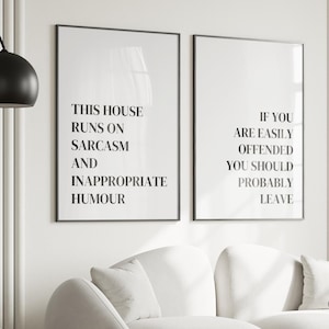 May include: Two rectangular wall art prints in thin black frames featuring black text on a white background. The left print reads THIS HOUSE RUNS ON SARCASM AND INAPPROPRIATE HUMOUR. The right print reads IF YOU ARE EASILY OFFENDED YOU SHOULD PROBABLY LEAVE.