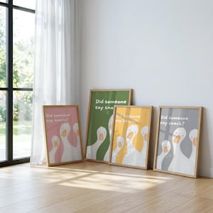Four framed prints lean against a white wall, each featuring three white geese and the text "Did someone say snack?" on backgrounds of pink, green, yellow, and gray.
