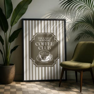 May include: Framed wall art with a black border featuring a coffee-themed design. The artwork has a brown background with white vertical stripes. The text "THE EARLY MORNING COFFEE CLUB" is displayed above a coffee cup illustration.