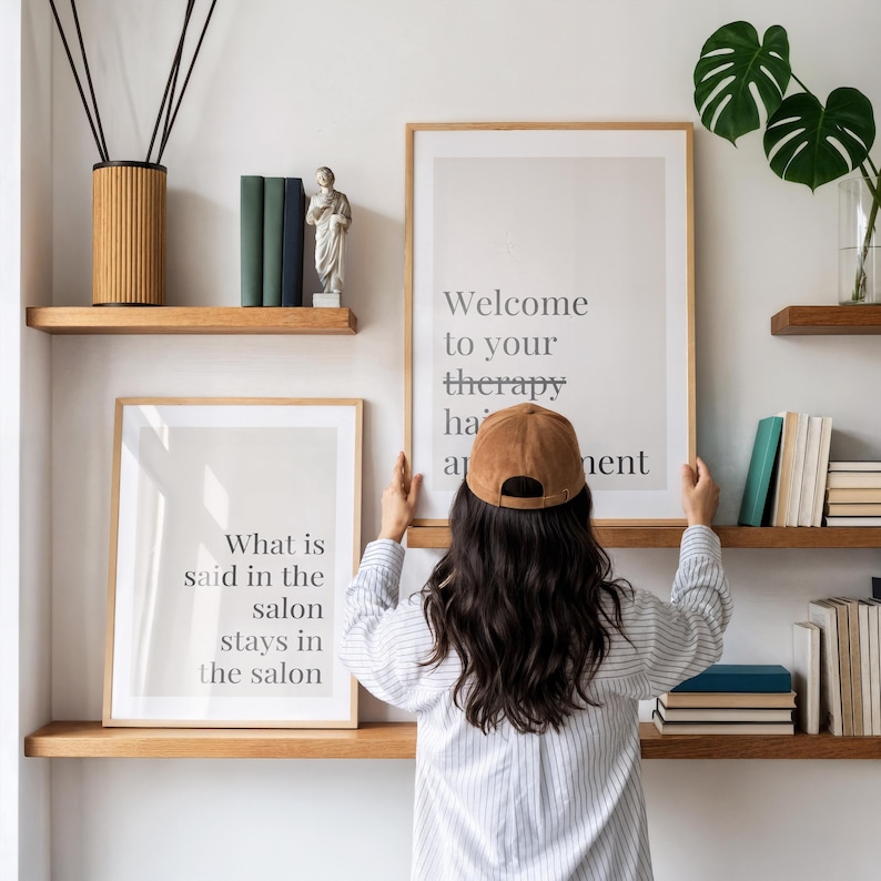 May include: Two framed wall art prints with text. One print reads Welcome to your therapy appointment and the other reads What is said in the salon stays in the salon. The prints are displayed on wooden shelves alongside books and a small statue.