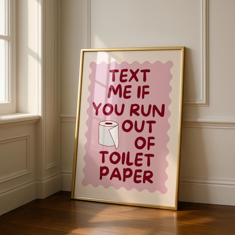 May include: A framed wall art print featuring a light pink scalloped rectangle background with dark red text that reads "TEXT ME IF YOU RUN OUT OF TOILET PAPER" and a simple line drawing of a white toilet paper roll centered in the middle.