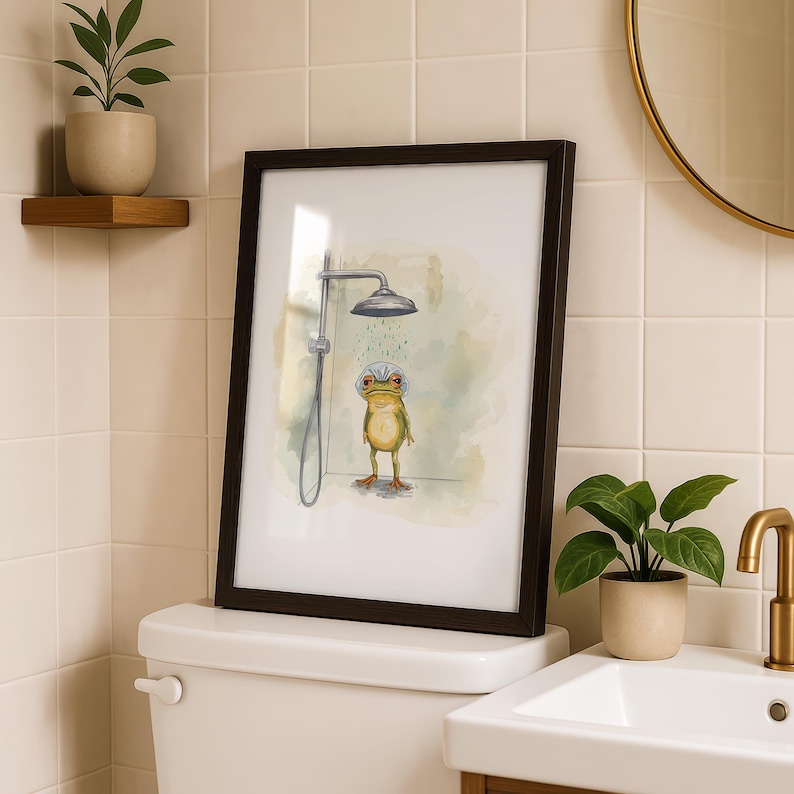 May include: A framed art print featuring a whimsical illustration of a frog taking a shower. The frog, with a shower cap, stands under a silver shower head. The artwork is set against a soft, watercolor-style background, framed in a dark brown frame.