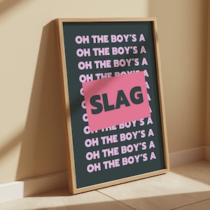 Könnte beinhalten: Ein gerahmter Kunstdruck mit dem Text "OH THE BOY'S A" in Rosa auf dunklem Teal-Hintergrund. Ein rosa Rechteck mit dem Wort "SLAG" ist überlagert. Der Rahmen ist hellholzfarben.