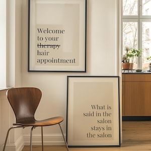 May include: Two framed wall art prints with black frames and beige backgrounds. The top print features the black text "Welcome to your therapy hair appointment". The bottom print features the black text "What is said in the salon stays in the salon".