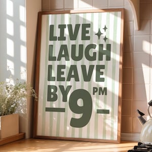 Peut inclure: Une affiche encadrée avec les mots "LIVE LAUGH LEAVE BY 9 PM" en vert foncé sur un fond à rayures vertes claires et blanches. L'affiche est dans un cadre en bois et est affichée dans une cuisine.