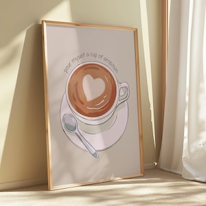 Puede incluir: Impresión artística enmarcada que presenta una taza de café con un diseño en forma de corazón en la espuma. La impresión incluye el texto "pour myself a cup of ambition". La obra de arte está sobre un fondo neutro.
