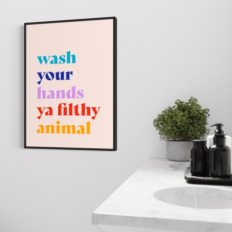 Puede incluir: Una l&aacute;mina enmarcada con fondo rosa claro que presenta el texto "wash your hands ya filthy animal" en l&iacute;neas apiladas. La palabra "wash" es azul verdoso, "your" es azul oscuro, "hands" es violeta claro, "ya filthy" es rojo y "animal" es naranja.