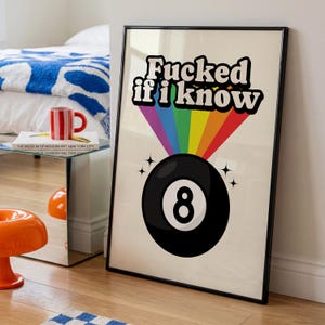 Op de afbeelding: Een ingelijste kunstprint met een zwarte 8-ball afbeelding onderaan en een regenboogkleurige straal die naar boven uitstraalt. Boven de regenboog staat de tekst Fucked if i know in dikgedrukte zwarte letters met een witte omlijning op een crèmekleur.