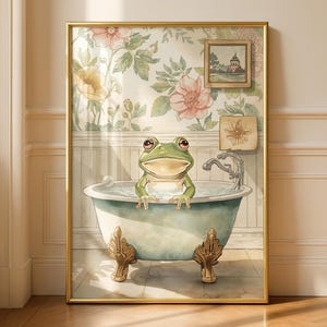 May include: A framed watercolour print shows a green frog in a vintage bathtub. The light blue tub has ornate gold feet. The background features floral wallpaper and small framed art pieces, creating a whimsical bathroom scene.