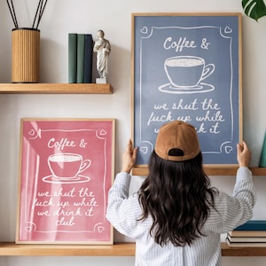 May include: Two framed art prints with coffee-themed text and illustrations. One print is pink, the other is blue. The text on the prints reads "Coffee &" and "we shut the f*ck up while we drink it club" and "we shut the f*ck up while we kit".
