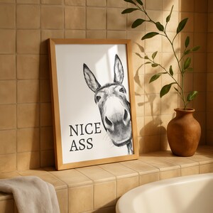 May include: A framed wall art print featuring a black and white charcoal-style illustration of a donkey's face looking forward. The text "NICE ASS" is printed in bold black capital letters on the left side of the white background within the frame.