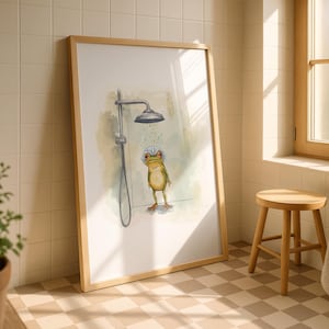 May include: A framed art print depicts a whimsical frog taking a shower. The frog, with a shower cap, stands under a shower head. The artwork is in a bathroom setting, with a wooden frame, a small wooden stool, and a window.