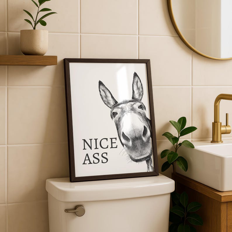 May include: A framed wall art print featuring a black and white illustration of a donkey head looking forward. The text NICE ASS is printed in black sans-serif capital letters on the left side of the donkey. The print is enclosed in a dark frame.